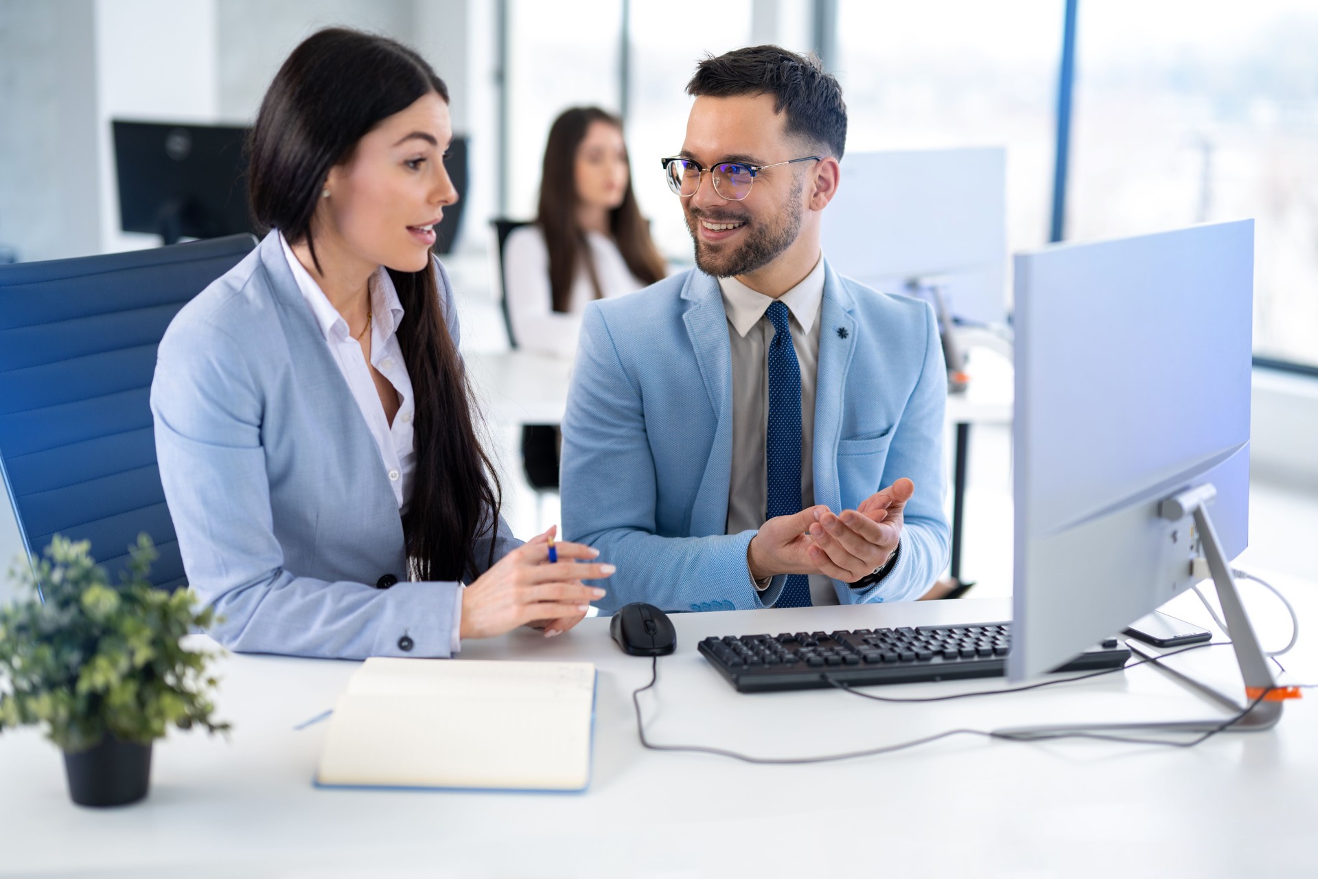 Business man and woman sitting in front of computer and working together on a project, discussing business strategy.